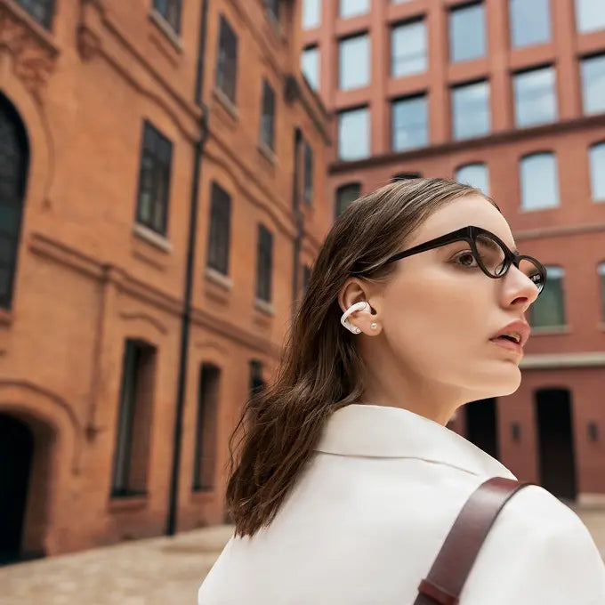 Woman wearing pearl white Shokz OpenDots 2 clip-on earbuds outdoors