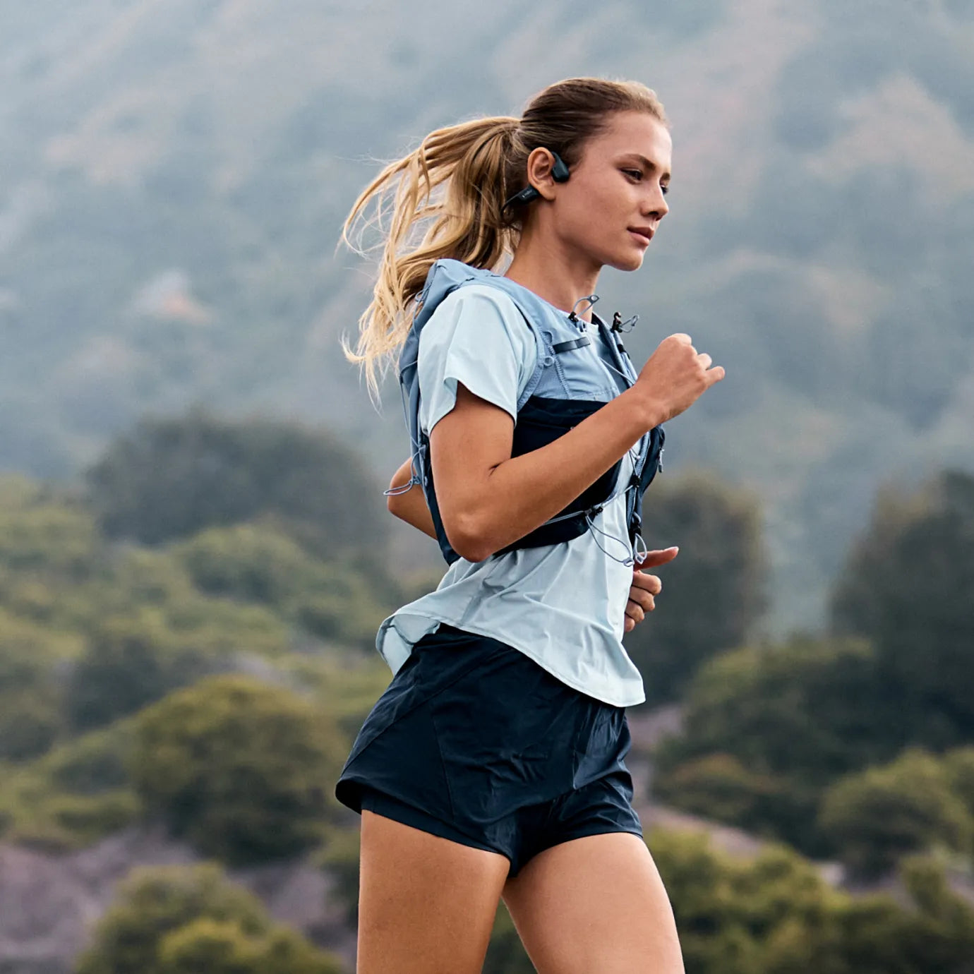 Runner wearing black Shokz OpenRun Pro 2 open-ear headphones on a trail